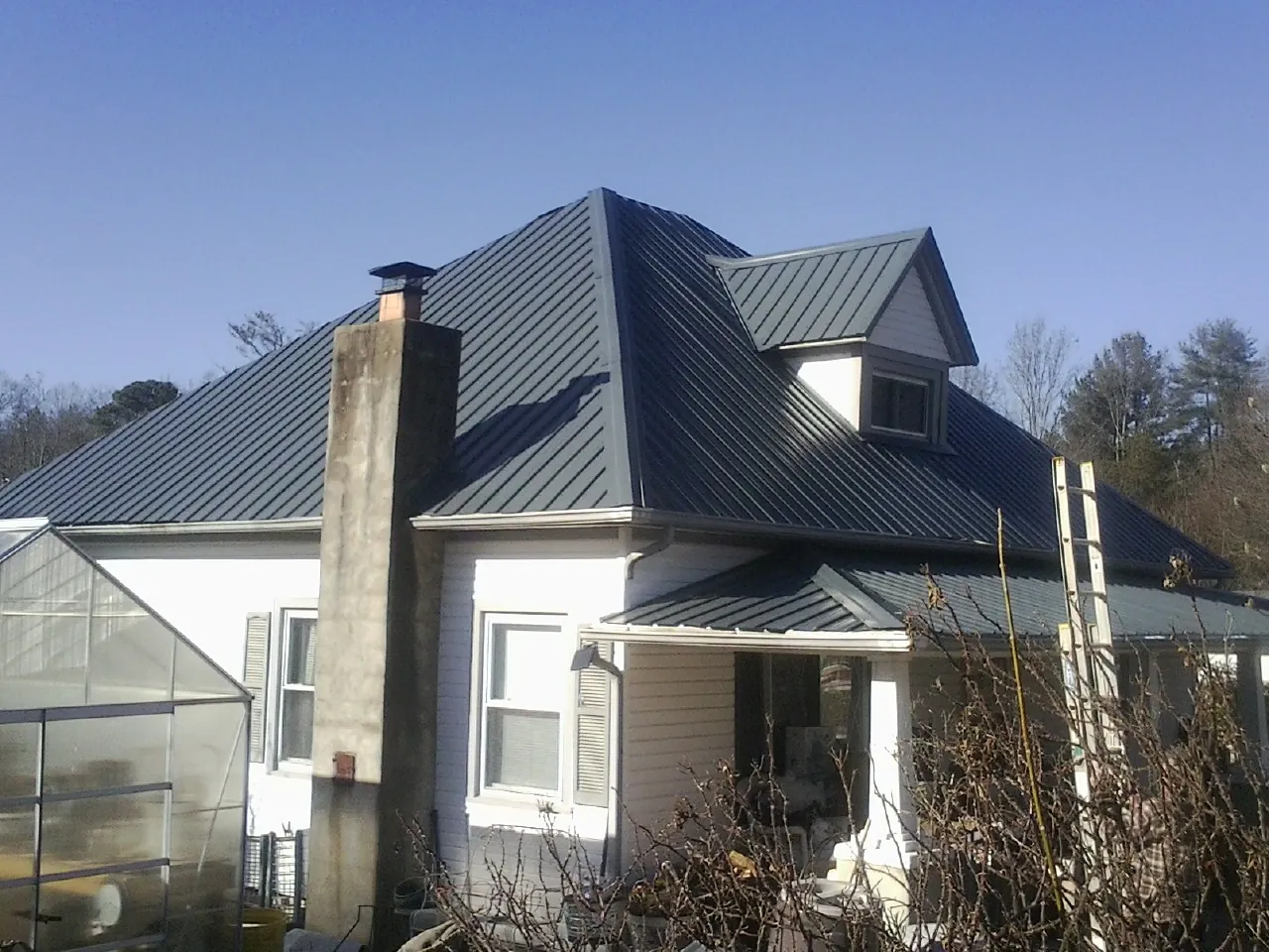 Dark blue standing seam metal roof on a white farmhouse with dormer — Slate & Tile Roof Repair by Roofing Brothers in Willow City