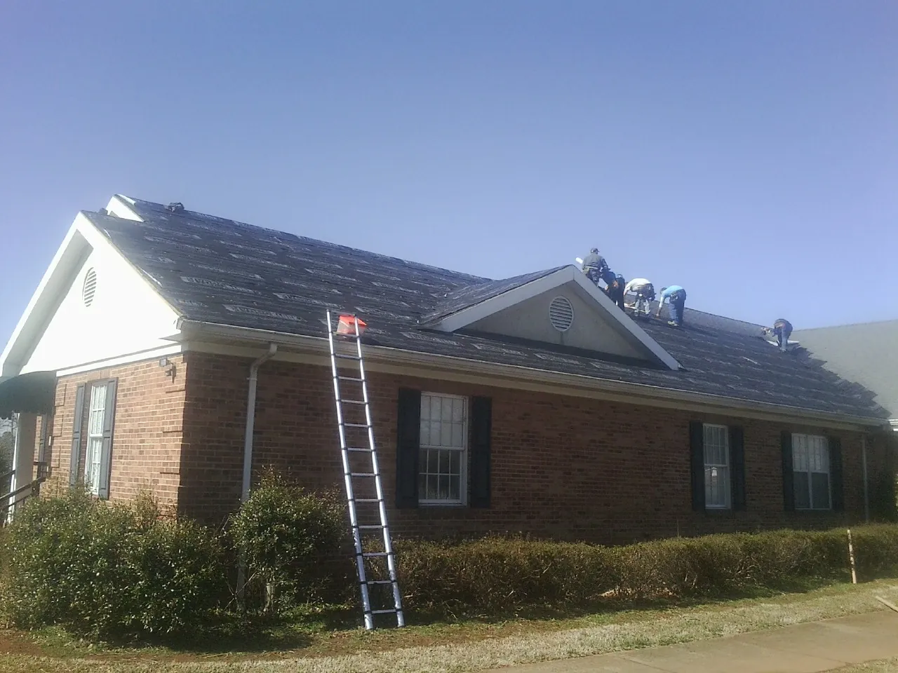 Crew tearing shingles off a brick ranch roof with a ladder set — Metal Roof Repair work by our crew in Willow City