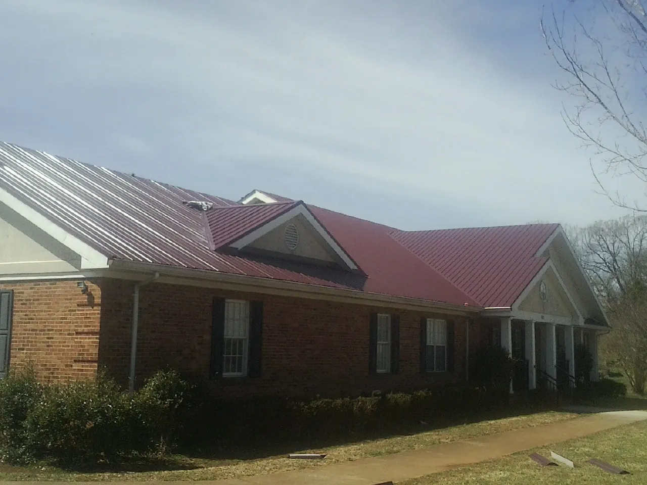Red metal roof with gabled entries on a long brick building, from a Hail Damage Roof Repair job in Willow City
