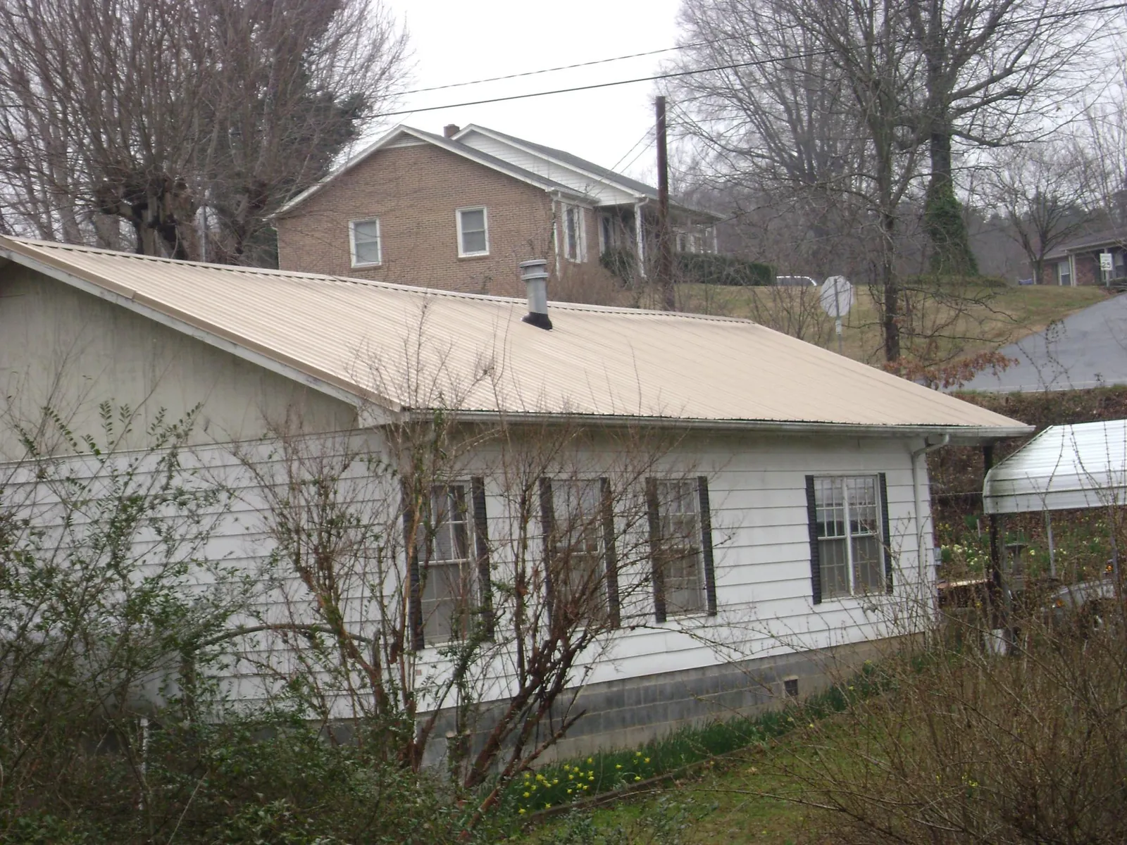 Tan metal roof on a white sided house set into a hillside — Commercial Roofing by Roofing Brothers in Willow City